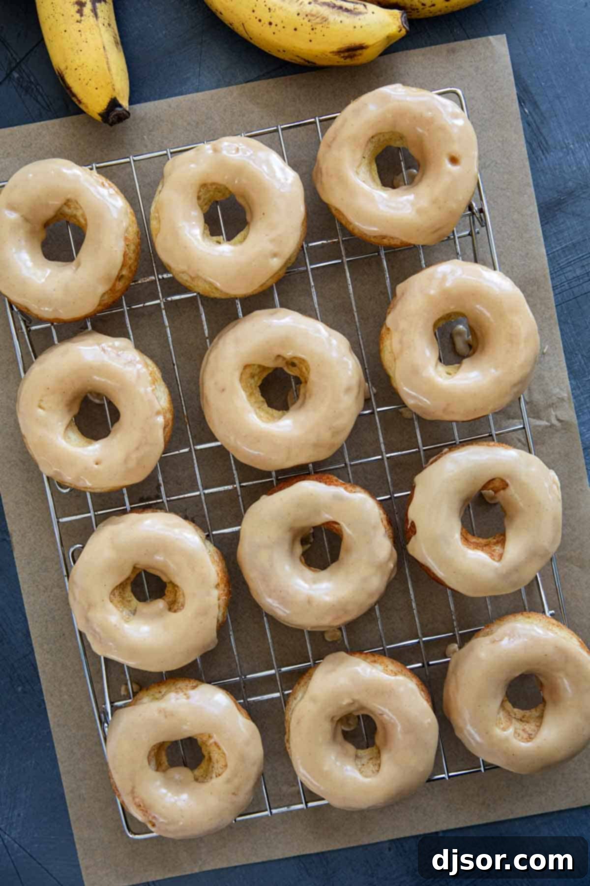 Banana donuts frosted with peanut butter icing on a cooling rack.