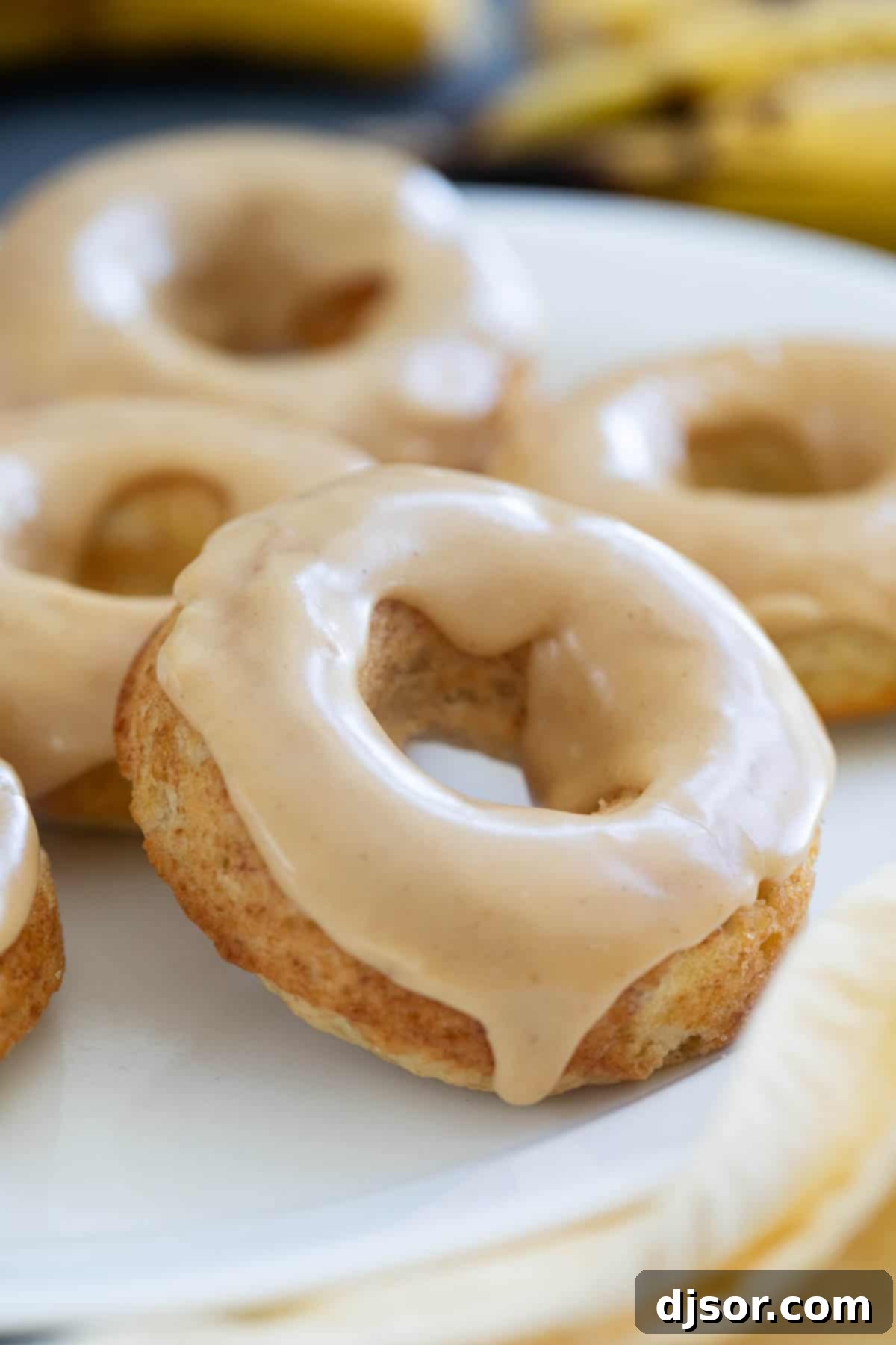 Baked banana donuts on a white plate, frosted with peanut butter icing.