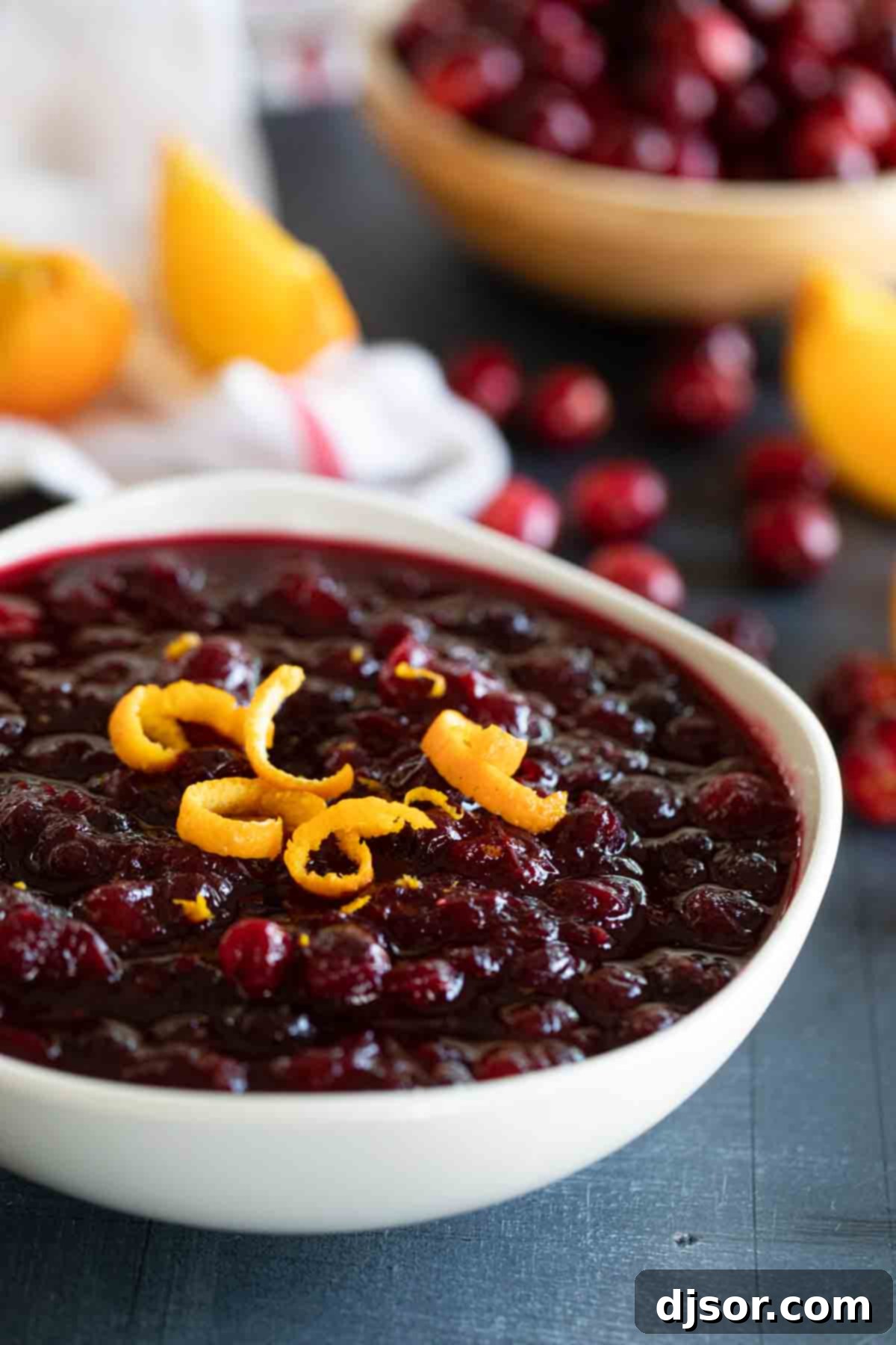 A pristine white bowl showcasing a generous serving of freshly made cranberry sauce, elegantly topped with delicate strips of orange zest for garnish.