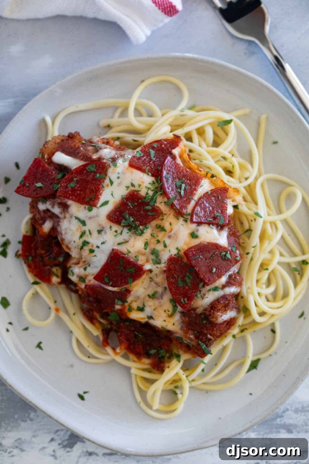 Chicken pepperoni served over a bed of buttered spaghetti on a white plate, ready to be enjoyed.