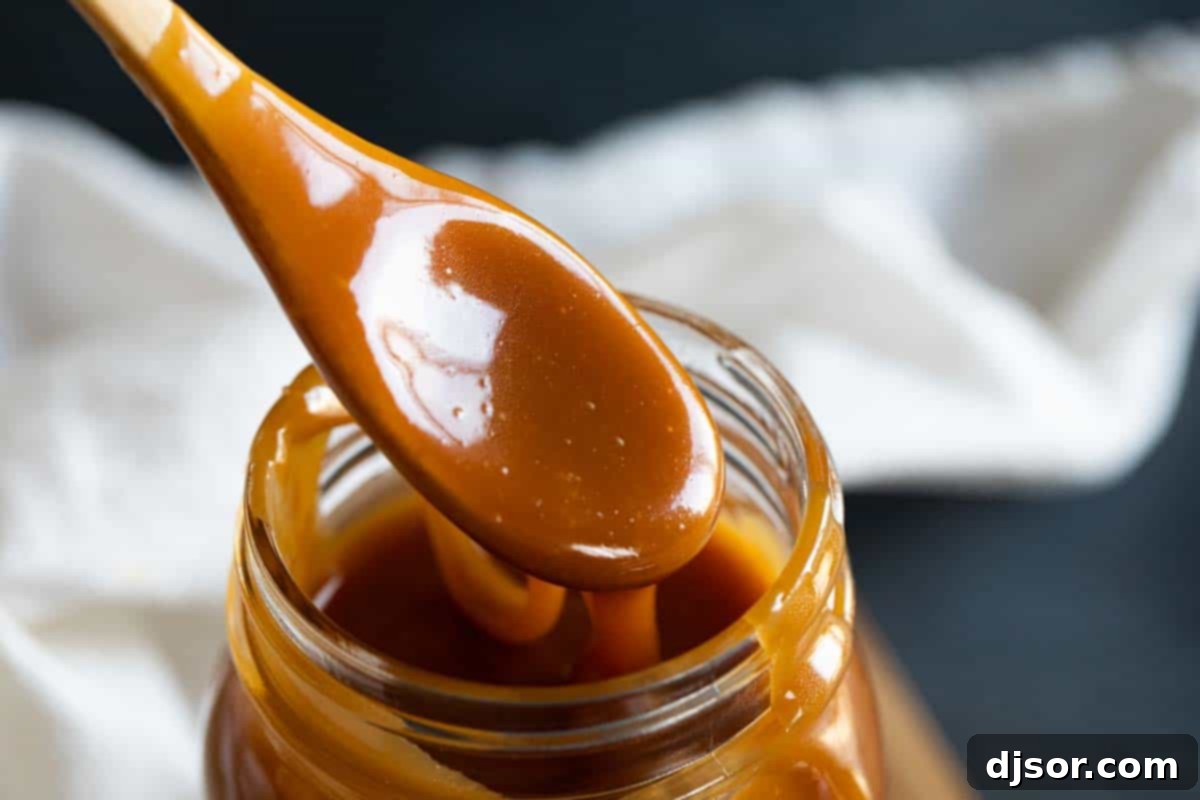 Homemade salted caramel sauce dripping lusciously from a spoon into a clear glass jar.