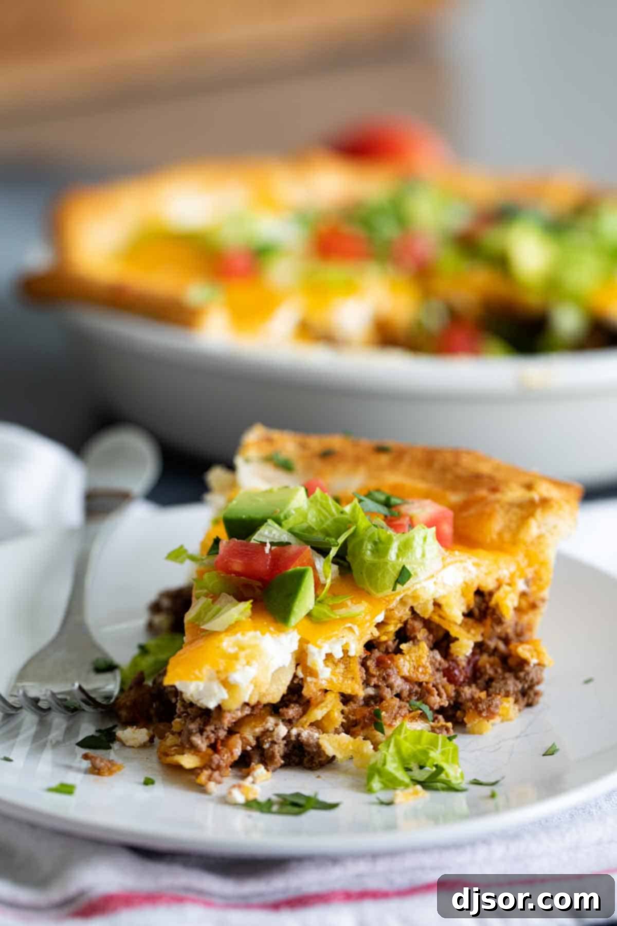 A Delicious Slice of Taco Pie a perfect slice of taco pie on a plate, showing layers of crust, beef, chips, sour cream, and cheese