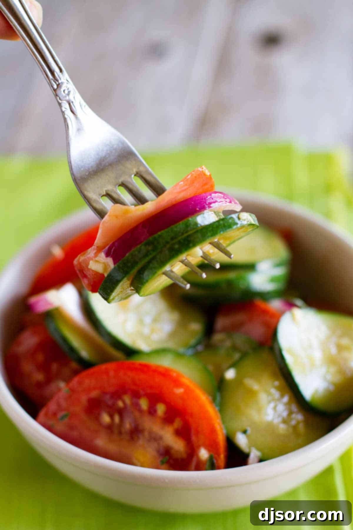 Close-up of a fork holding a bite of zucchini salad with tomatoes and red onion, highlighting the fresh ingredients and vibrant colors.