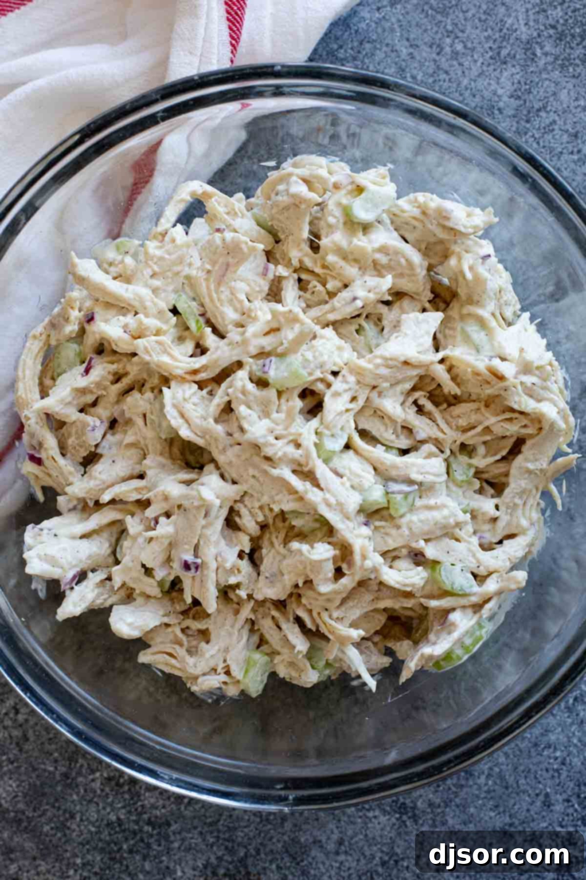 Classic chicken salad with fresh celery and red onions presented in a clear glass bowl, showcasing its delicious texture.