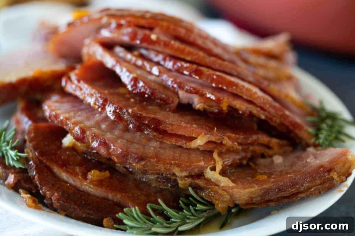 Crock Pot Ham: Your easiest path to a moist and flavorful holiday centerpiece. Succulent slices of Crock Pot Ham on a serving plate, garnished with fresh rosemary for a holiday spread.