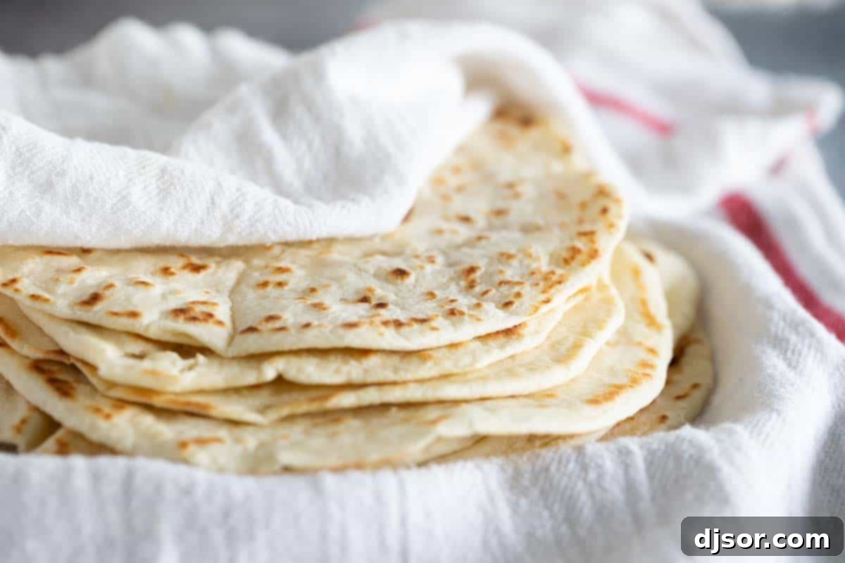 Homemade flour tortillas stacked on each other under a white towel, showcasing their soft, inviting texture.