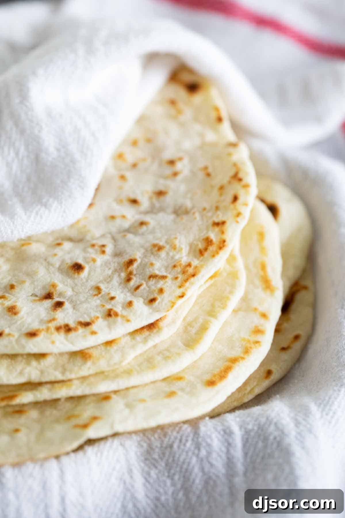 Stack of homemade flour tortillas wrapped in a towel, keeping them warm and soft.