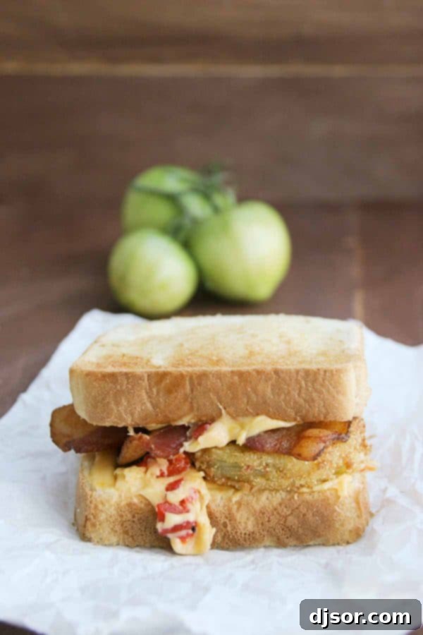 A close-up of a delectable Fried Green Tomato Sandwich, showcasing its layers of crispy fried green tomatoes, melted pimiento cheese, and crunchy bacon, all nestled between slices of golden Texas toast.