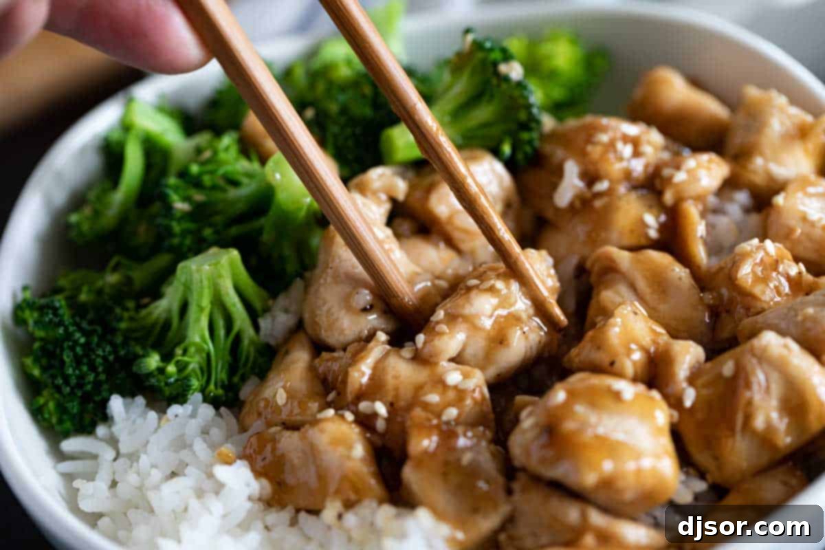 An easy and tasty weeknight meal, these Teriyaki Chicken Bowls are on the table in no time at all and are great for those nights that you don’t feel like cooking. Chopsticks picking up a piece of glazed teriyaki chicken from a bowl, highlighting its tender texture.