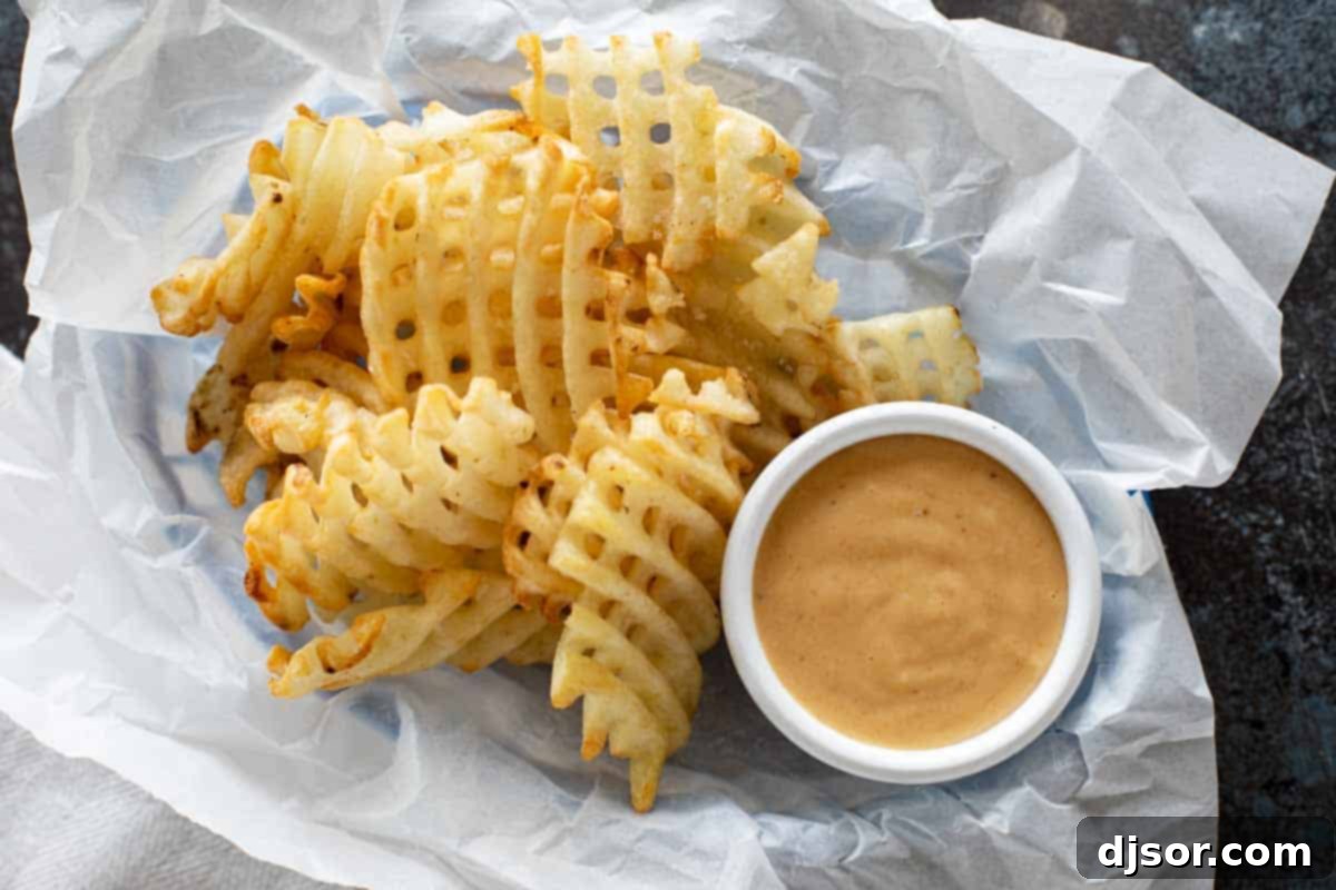 Delicious homemade Chick-fil-A sauce served with golden waffle fries and crispy chicken nuggets. Basket with waffle fries and chick fil a sauce