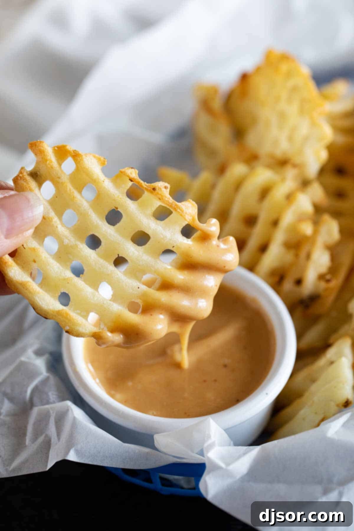 Perfectly golden waffle fry being dipped into the creamy, homemade Chick-fil-A sauce. Dipping a crispy waffle fry into homemade chick fil a sauce