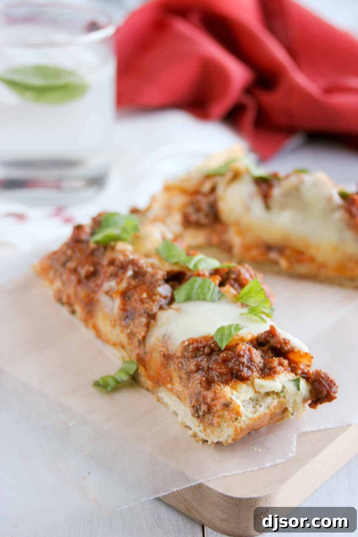 Lasagna Bread Pizza - French bread pizza meets lasagna for this easy pizza dinner. Slices of Lasagna Bread Pizza on a wooden cutting board, showcasing melted cheese, rich meat sauce, and crispy French bread