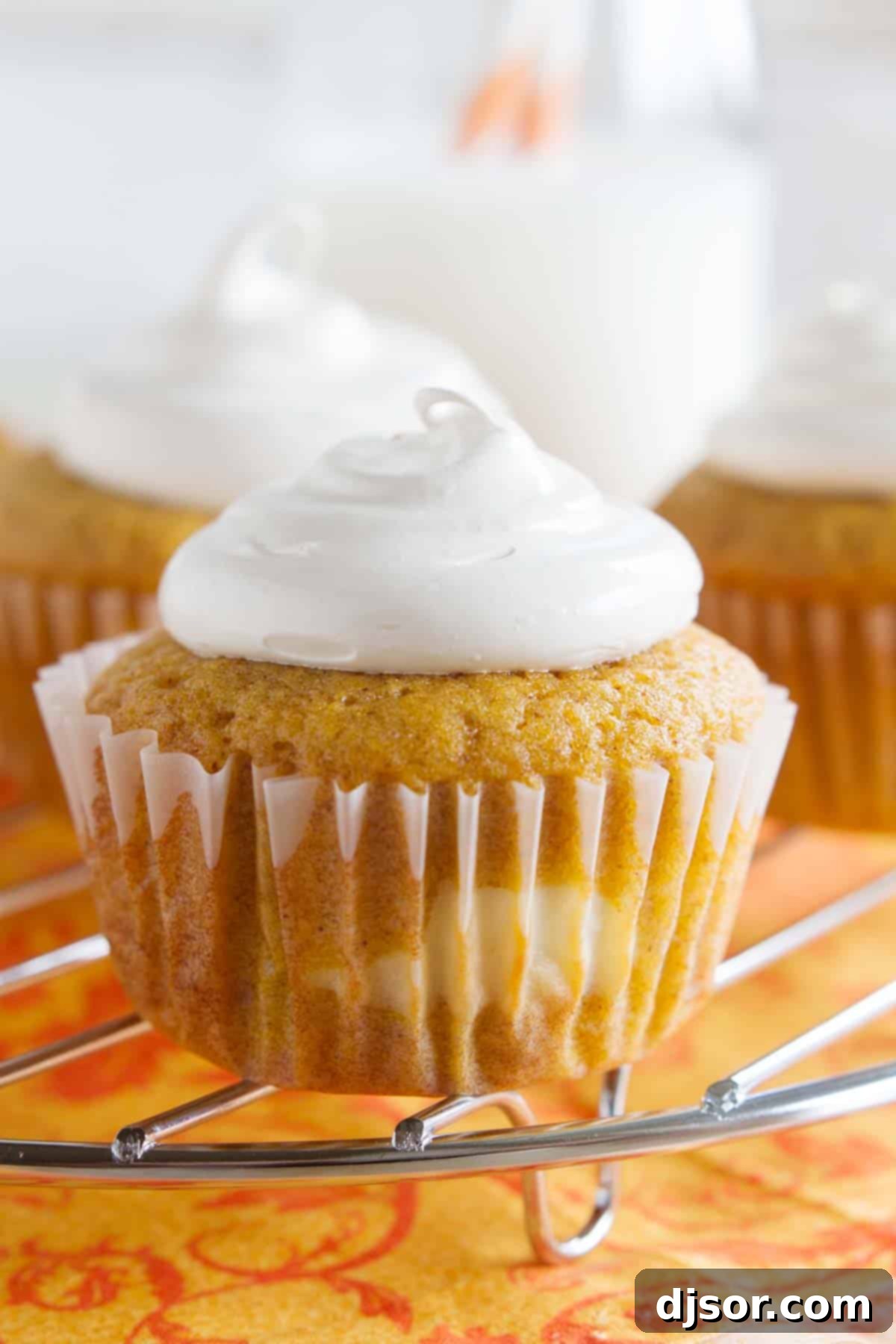 Pumpkin Cheesecake Cupcakes on a cooling rack over an orange cloth, showcasing their beautiful tops before frosting.