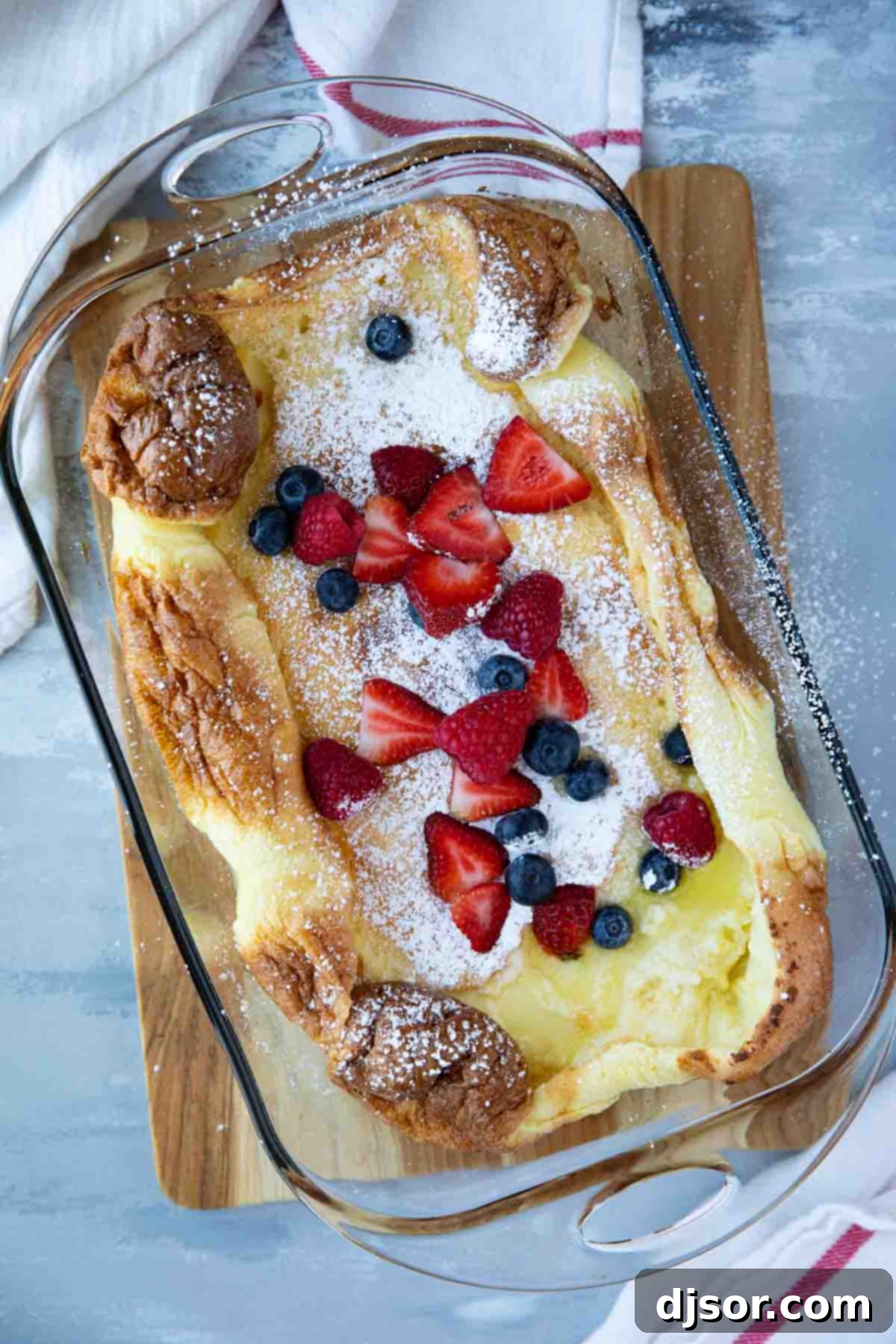 Top-down view of a beautifully puffed Dutch Baby in a glass baking dish, generously topped with an assortment of fresh berries