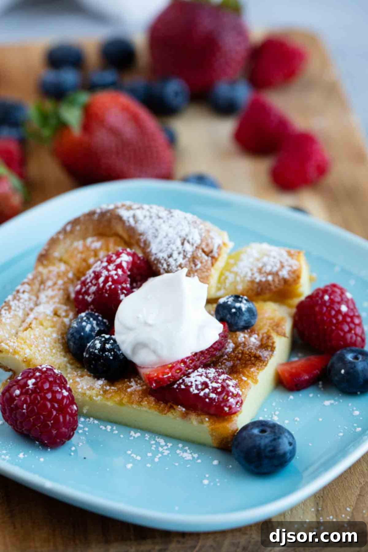 A delectable slice of Dutch Baby, elegantly topped with fresh mixed berries and a dollop of fluffy whipped cream, invitingly presented