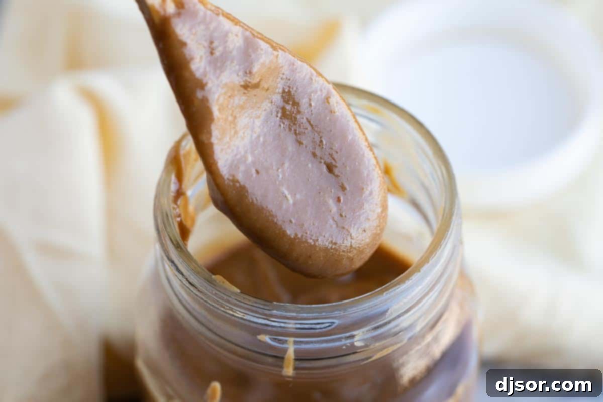 A glass jar filled with freshly made, creamy peanut sauce, with a small spoon resting inside, ready for storage or serving.