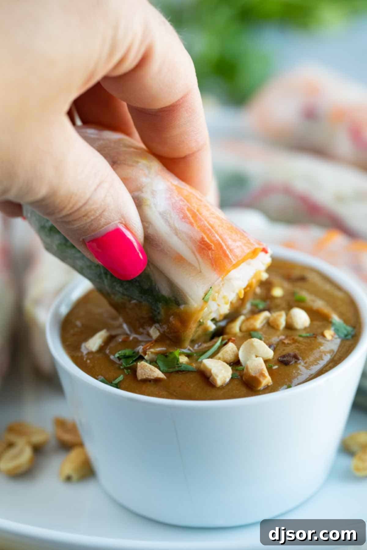 A hand dipping a fresh spring roll into a bowl of creamy homemade peanut sauce, showcasing its perfect dipping consistency.