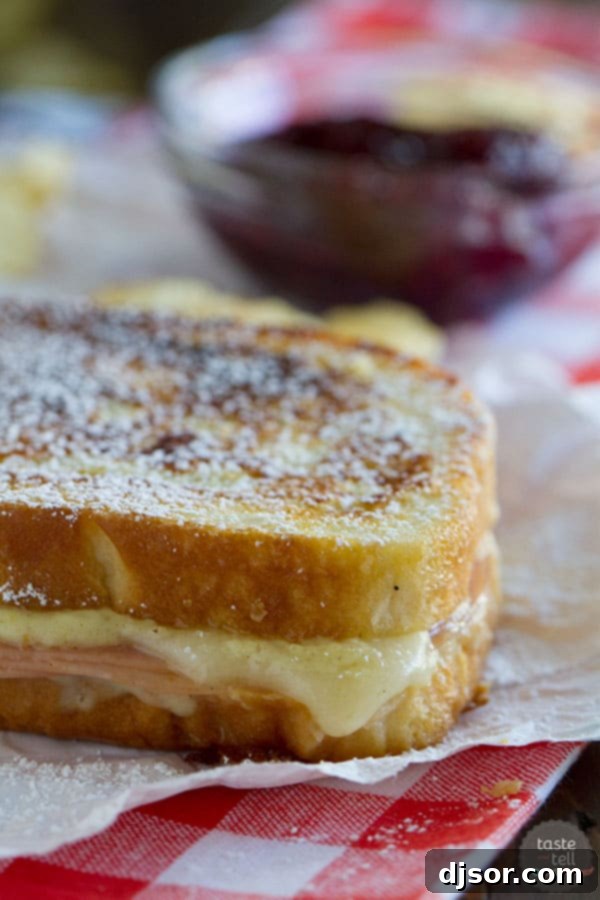 Monte Cristo Croque Monsieur 2 A golden brown Monte Cristo-style Croque Monsieur sandwich, topped with powdered sugar and a side of raspberry jam, showcasing melted cheese and ham inside.