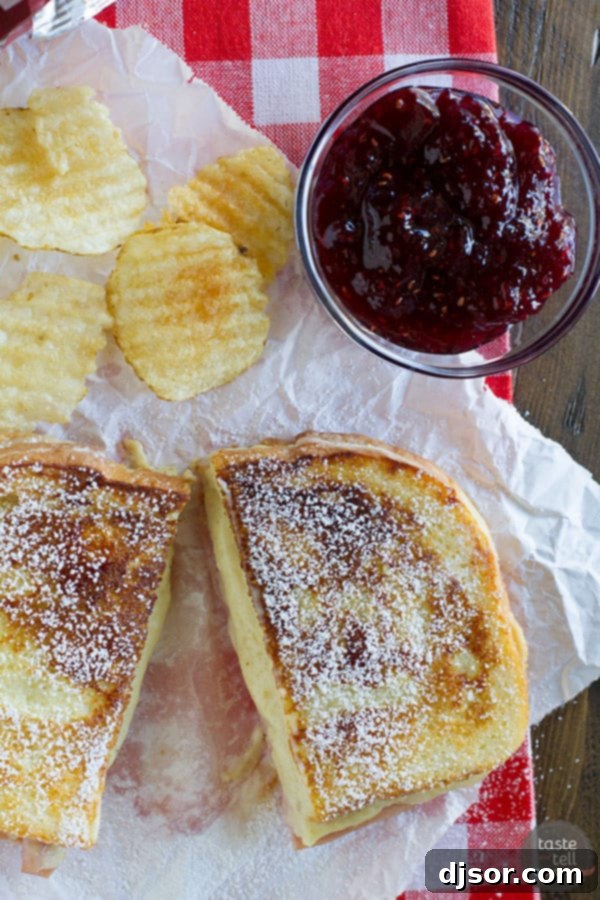 Monte Cristo Croque Monsieur 4 A stack of golden Monte Cristo-style Croque Monsieur sandwiches, with a hint of powdered sugar and a small bowl of vibrant raspberry jam, ready to be served.