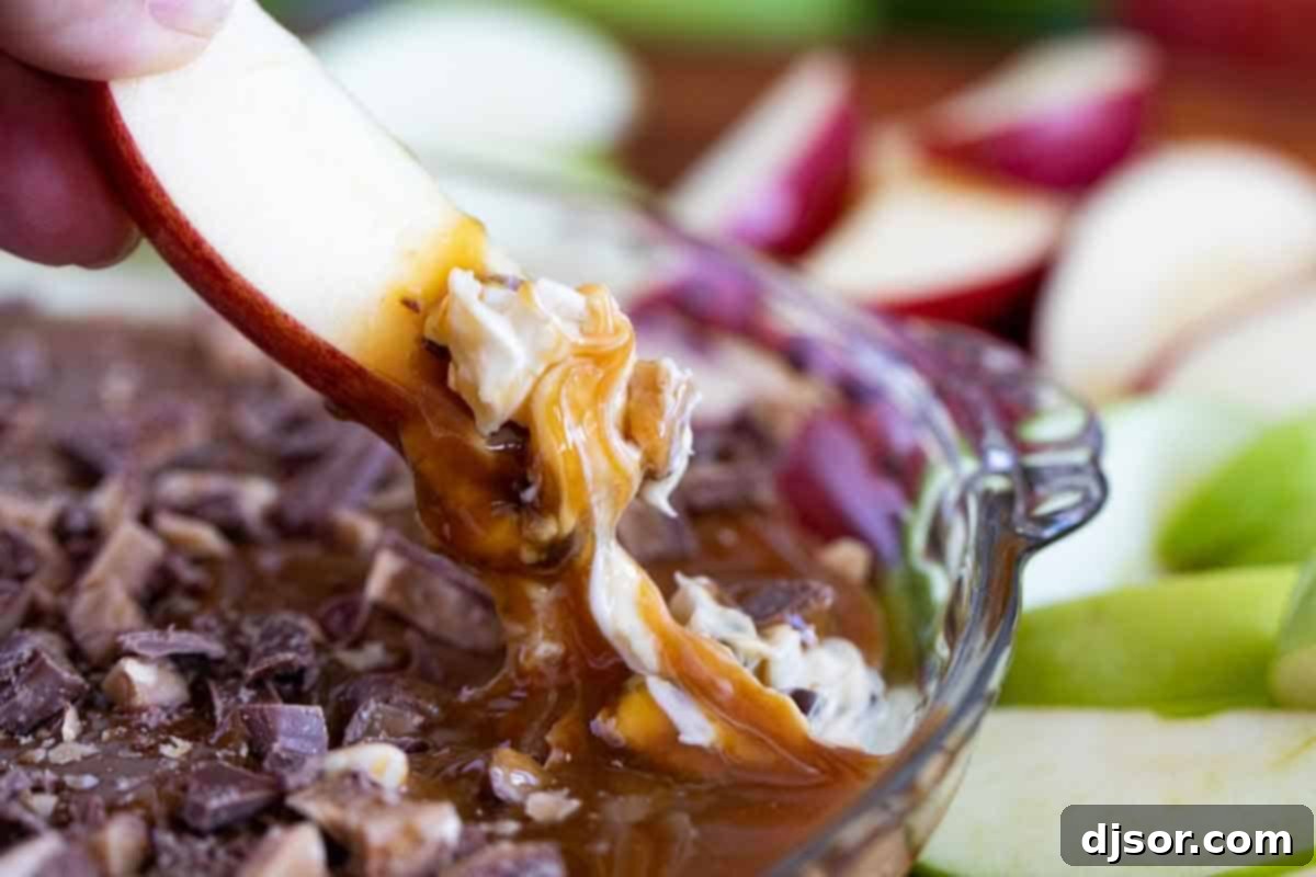 A crisp green apple slice being dipped into a luscious caramel apple dip, showcasing its creamy texture and rich toppings.