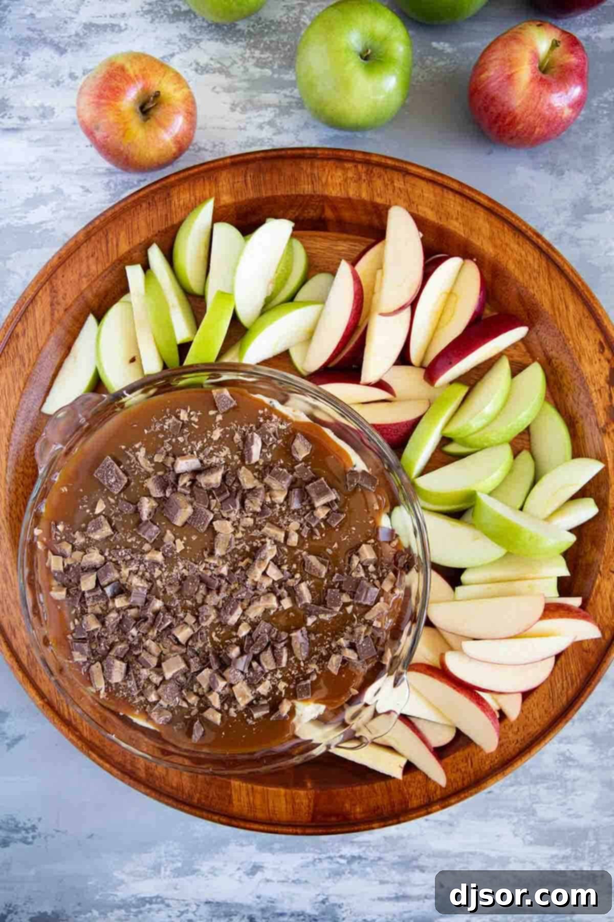 A vibrant Caramel Apple Dip surrounded by an assortment of red and green sliced apples, perfectly arranged for dipping.