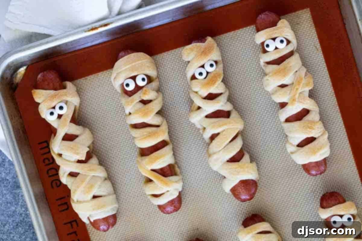 Perfect for Halloween or for a spooky dinner or lunch, these Mummy Hot Dogs are kid approved and couldn’t be easier! Mummy hot dogs on a baking sheet, golden brown and ready to serve.