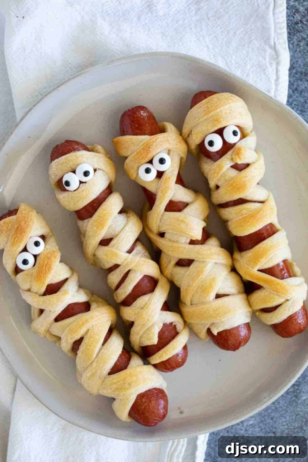 Perfect for Halloween or for a spooky dinner or lunch, these Mummy Hot Dogs are kid approved and couldn’t be easier! Mummy hot dogs with candy eyes on a plate, ready to be served with dipping sauces.
