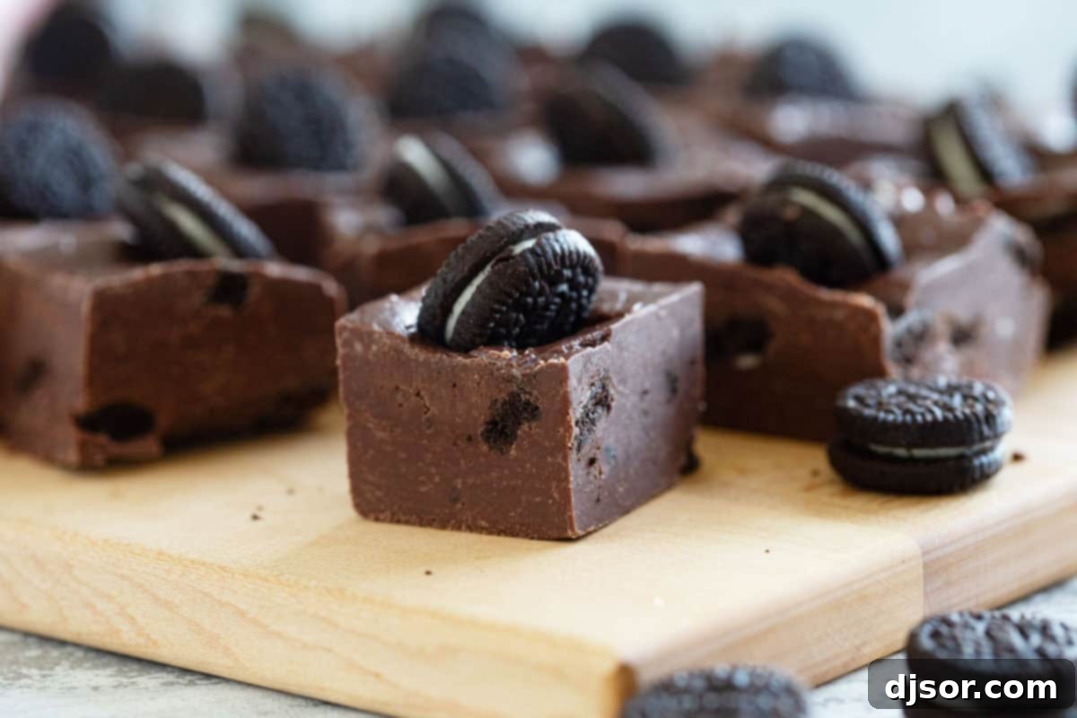 Ultimate Oreo Fudge Delight 2 A delectable square of Oreo Fudge resting on a rustic wooden cutting board, showcasing its creamy texture and embedded cookie pieces.
