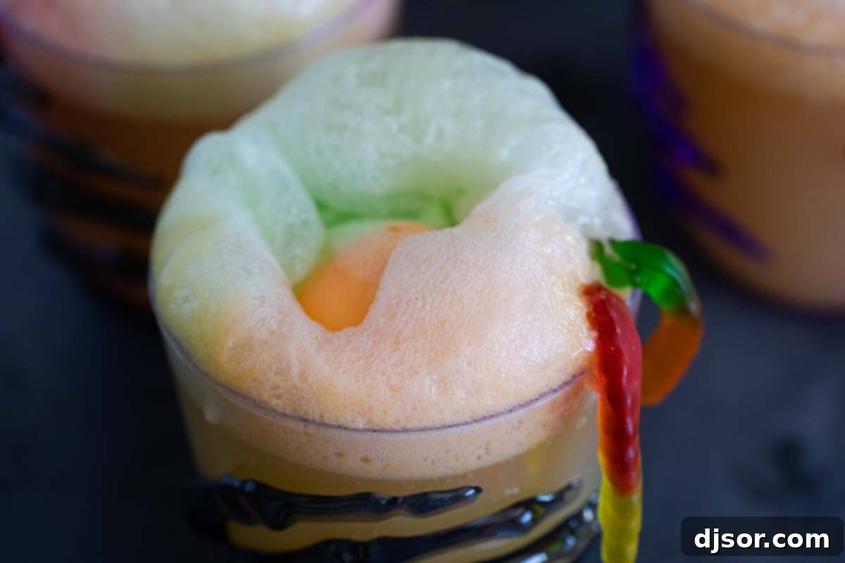Halloween Drink with Gummy Worms A festive Halloween drink elegantly presented in a glass, crowned with a scoop of colorful sherbet and adorned with a playful gummy worm for extra spookiness.