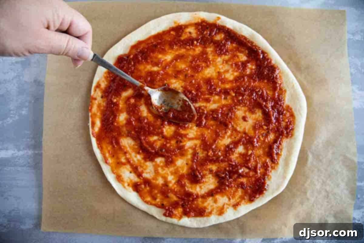 The perfect layer of homemade pizza sauce ready for toppings on a pizza base. Spreading pizza sauce on pizza crust.