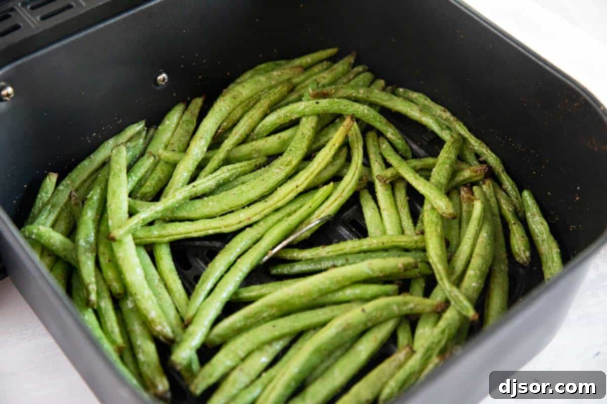 Green beans ready for air frying. Fresh green beans arranged in a single layer inside an air fryer basket, ready for cooking.