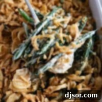 A close-up of a serving spoon holding a generous portion of homemade green bean casserole, showcasing its creamy texture and crispy onion topping.