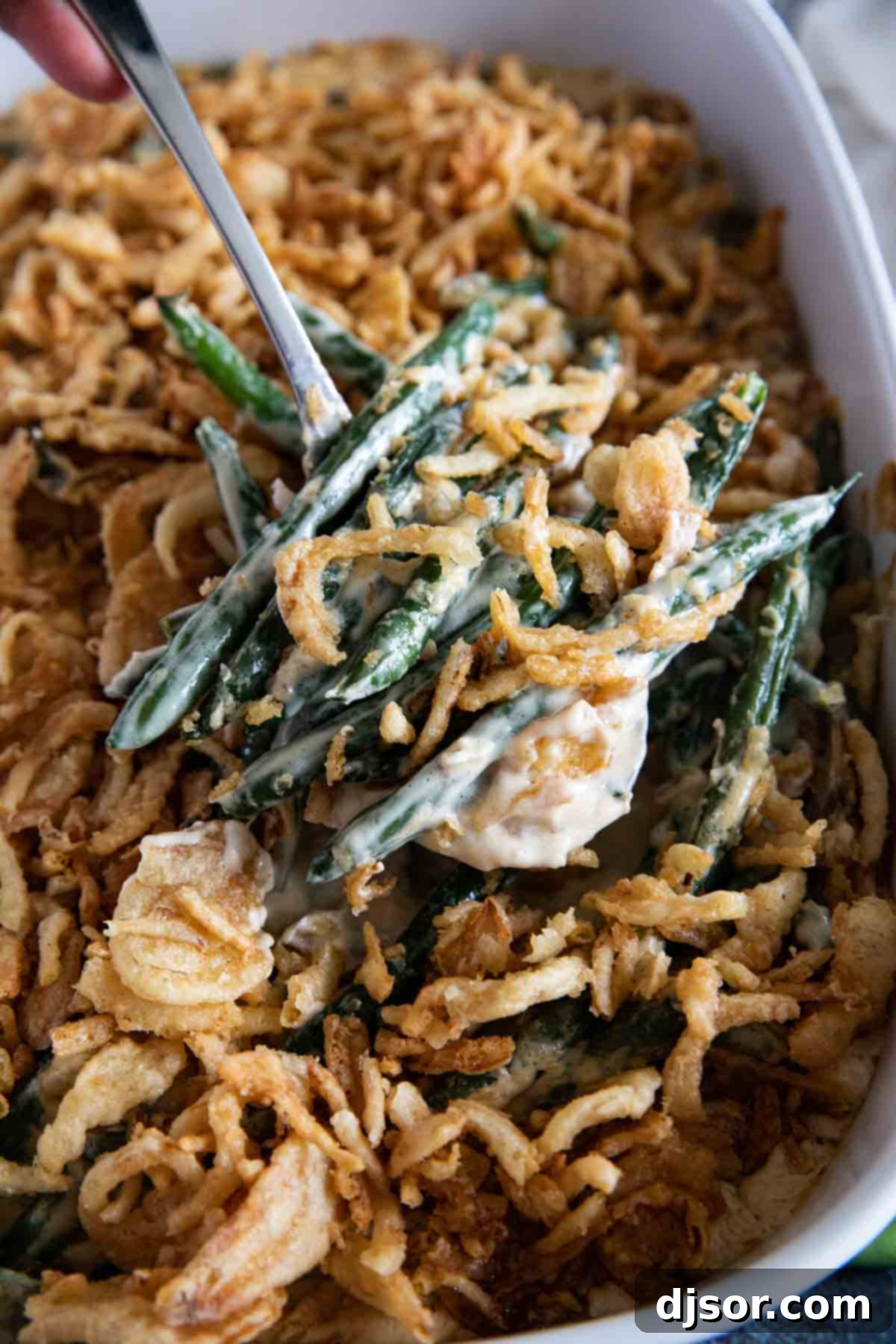 A close-up of a serving spoon holding a generous portion of homemade green bean casserole, showcasing its creamy texture and crispy onion topping.