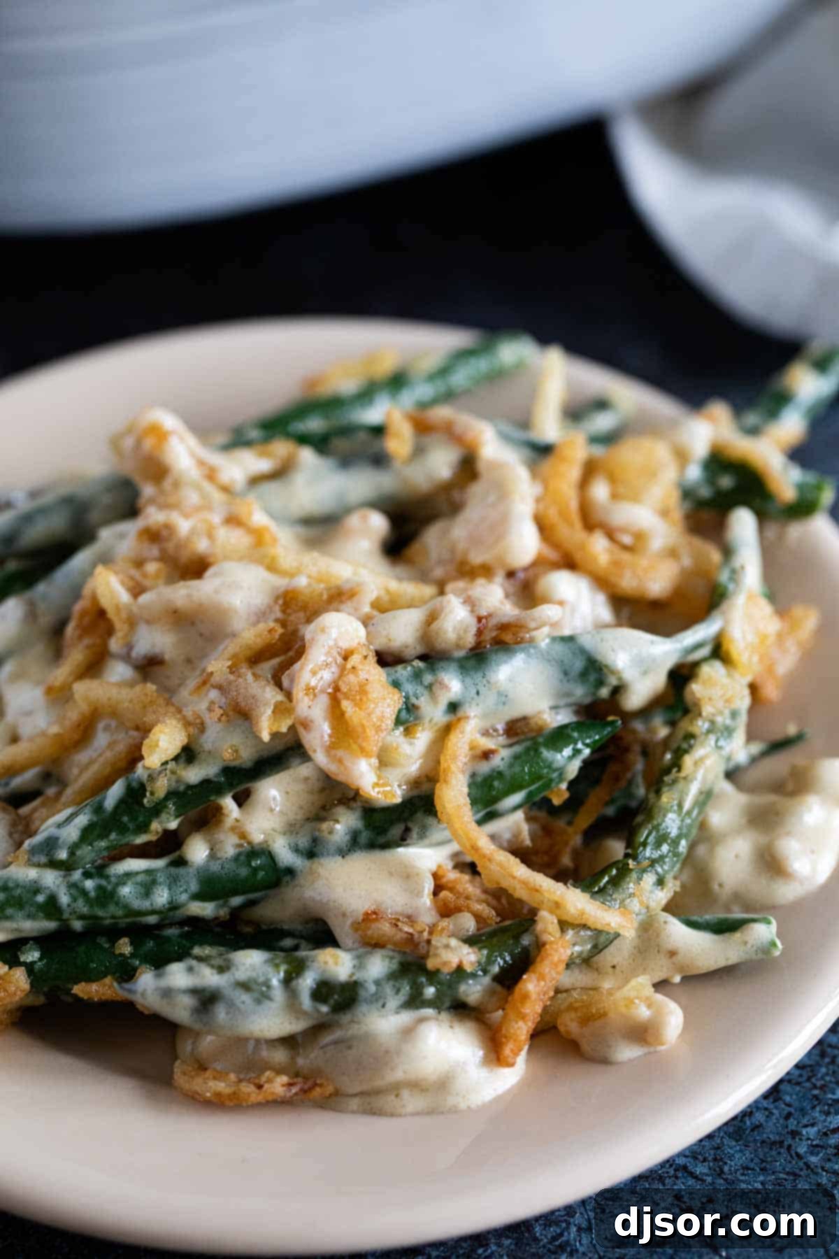 A white plate featuring a generous serving of homemade green bean casserole, perfectly garnished with a crunchy topping of golden fried onions.