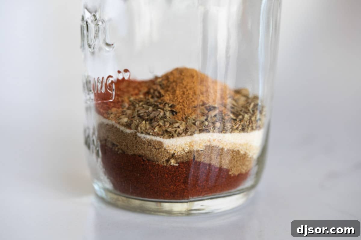 All the spices neatly arranged in a jar, showcasing the beauty of the raw ingredients before they are blended. Individual spices layered on top of each other in a small glass jar before mixing.