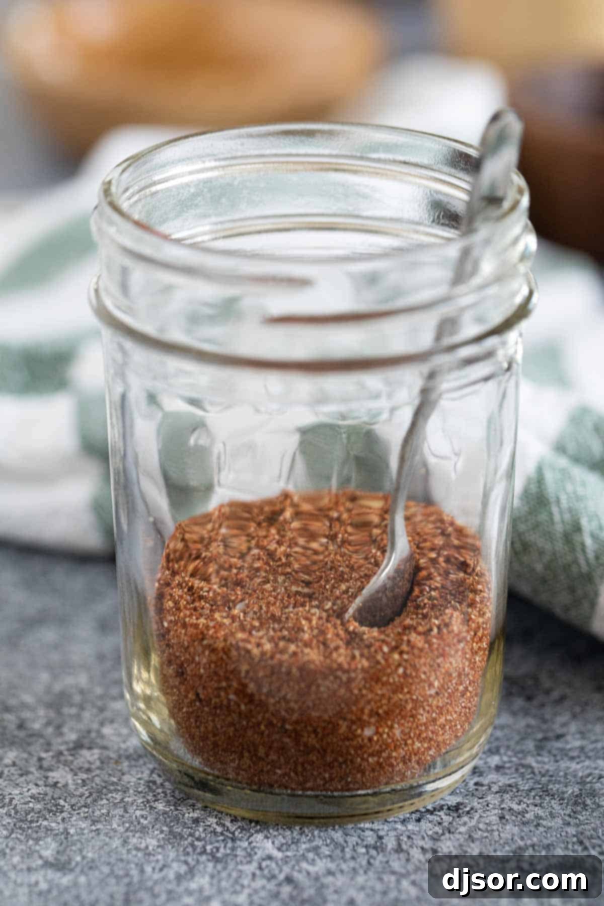 A beautifully simple shot of homemade taco seasoning, perfectly blended and ready in a jar. A small jar of homemade taco seasoning with a spoon inside.