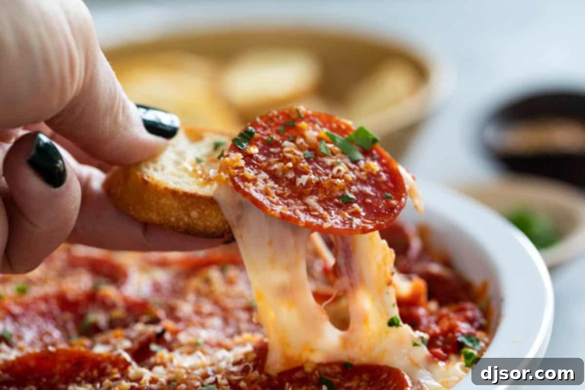 A delicious slice of toasted baguette covered in melted pepperoni pizza dip, showing a perfect cheese pull.