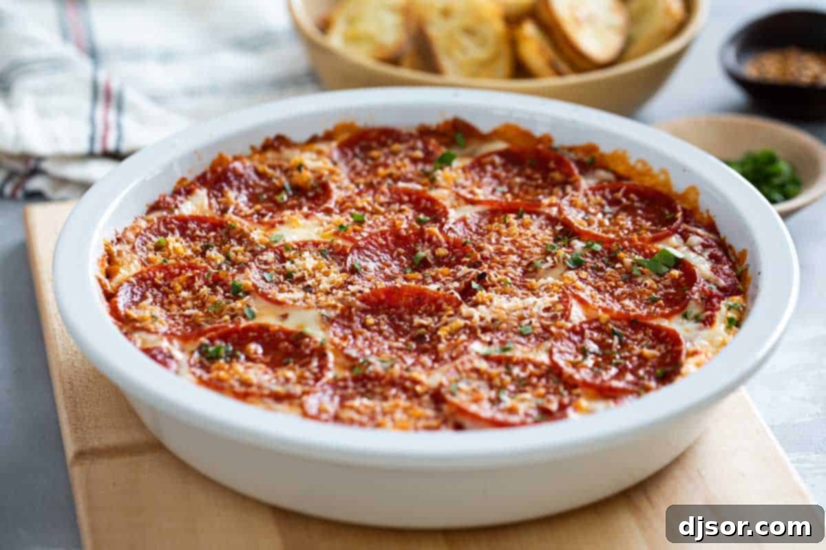 A bubbling Pepperoni Pizza Dip in a white pie dish, surrounded by toasted baguette slices, ready for serving.