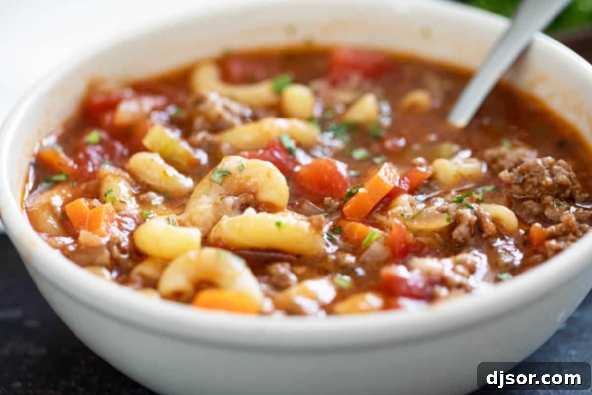 A steaming bowl of classic Hamburger Soup, brimming with macaroni, ground beef, and colorful vegetables, garnished with fresh herbs.