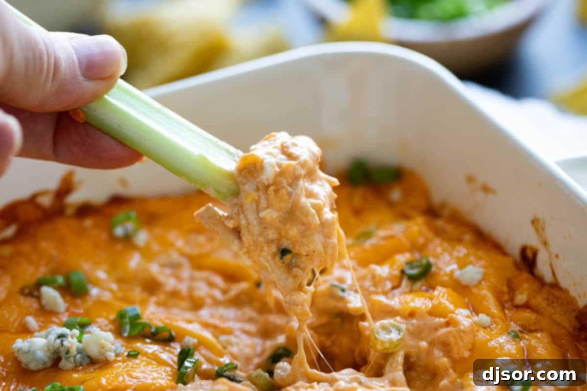 Dipping a celery stick into buffalo chicken dip. A classic game day appetizer, this Buffalo Chicken Dip is so popular for a reason! Filled with all of your favorite buffalo chicken flavors, this dip is super easy to make and always disappears.