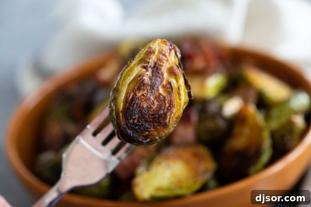 The tastiest - and easiest - way to prepare Brussels sprouts, these Roasted Brussels Sprouts are always a hit. They only take a few minutes to prepare, and everyone loves them. A single halved Brussels sprout on the tines of a fork, highlighting its roasted texture and inviting appearance.