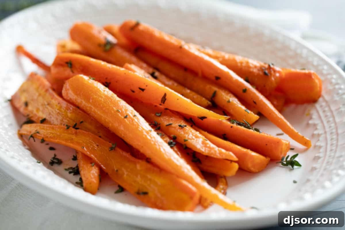 White serving dish filled with perfectly oven-roasted carrots, garnished with fresh thyme leaves, ready to serve.