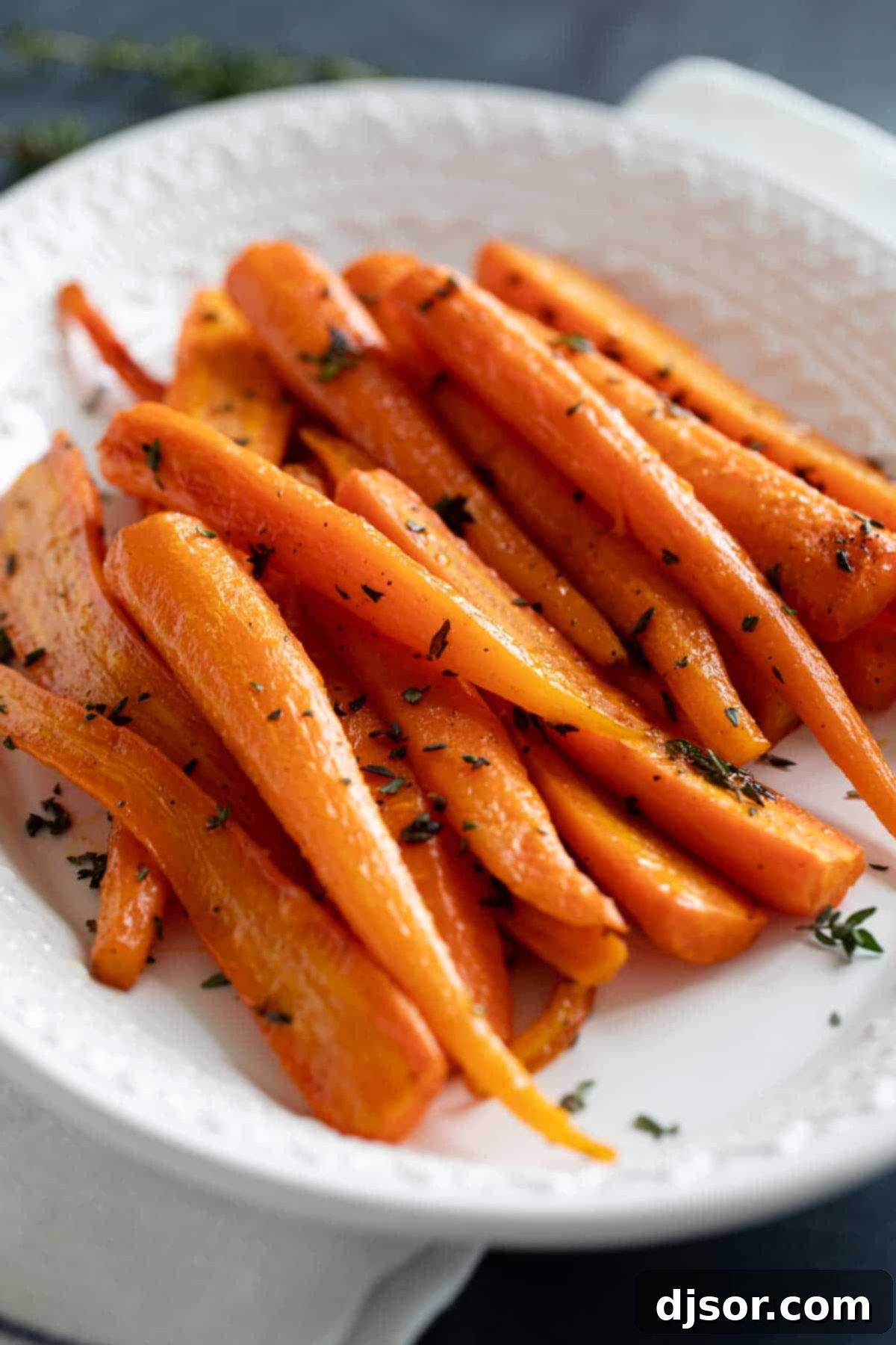 A close-up shot of vibrant orange oven roasted carrots, perfectly caramelized and sprinkled with fresh green thyme, served in a rustic white dish.