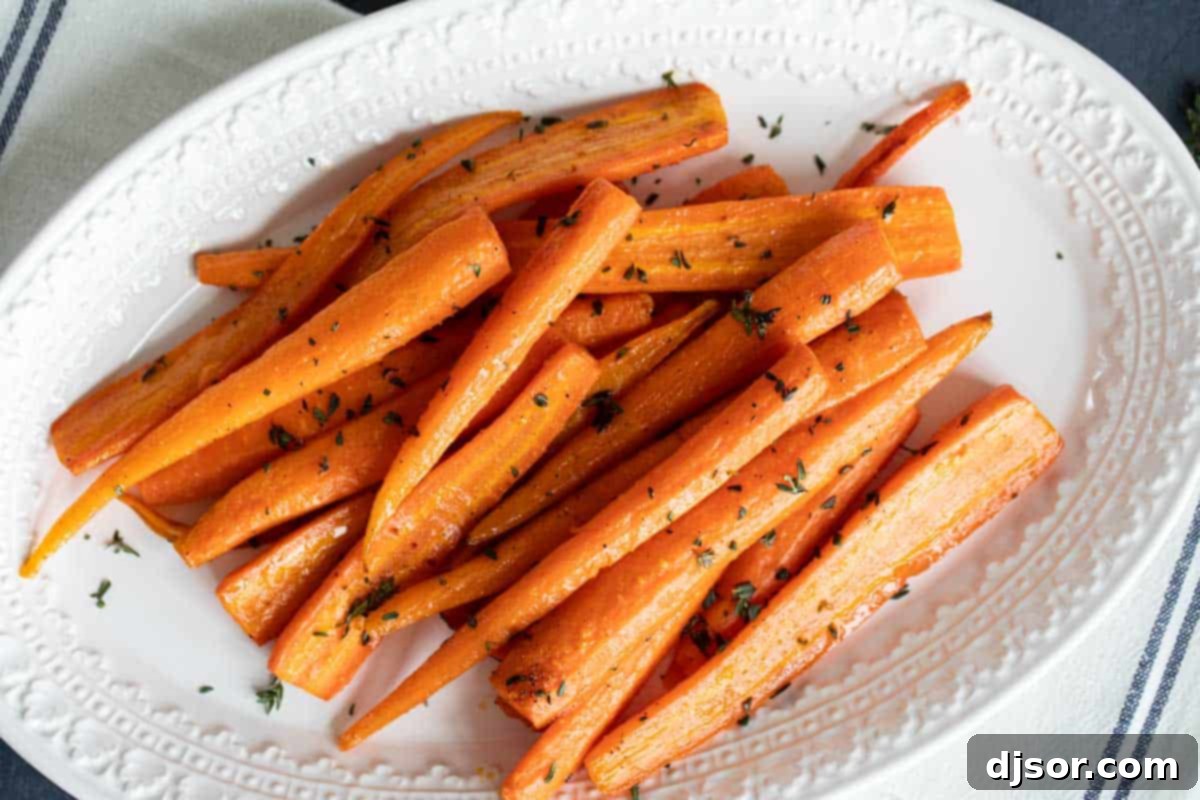 A simple white serving dish brimming with golden oven roasted carrots, garnished with fresh thyme, ready to be enjoyed as a flavorful side dish.