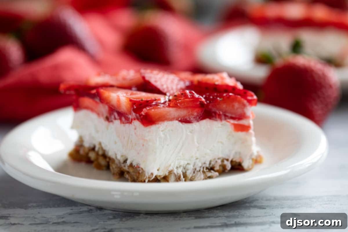 Sweet and salty, this Strawberry Pretzel Salad is as pretty as it is delicious. Serve it as a side dish or a dessert - either way, it’s always a hit! Slice of Strawberry Pretzel Salad with fresh strawberries in the background, showcasing its vibrant layers.