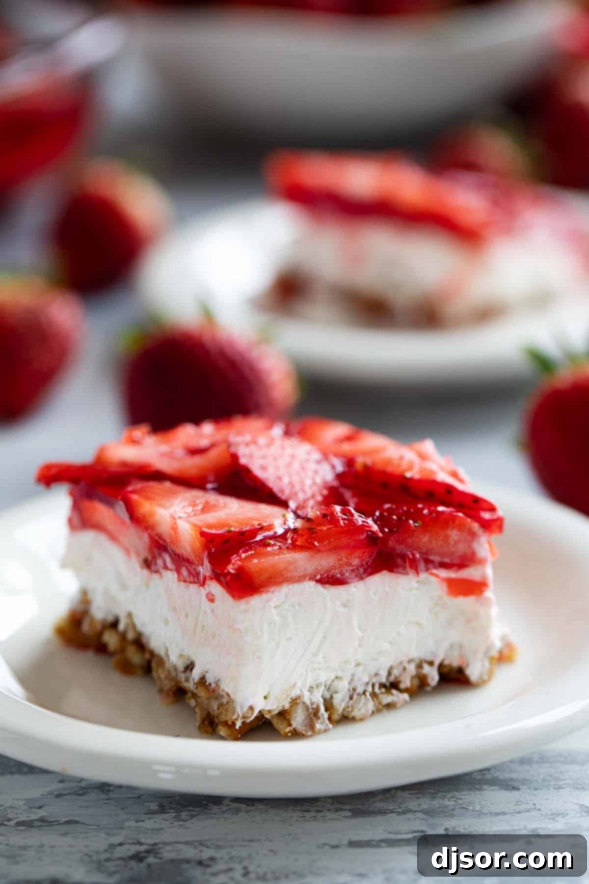 Sweet and salty, this Strawberry Pretzel Salad is as pretty as it is delicious. Serve it as a side dish or a dessert - either way, it’s always a hit! Slice of Strawberry Pretzel Salad on a plate with another slice in the background, showing the perfect layers.
