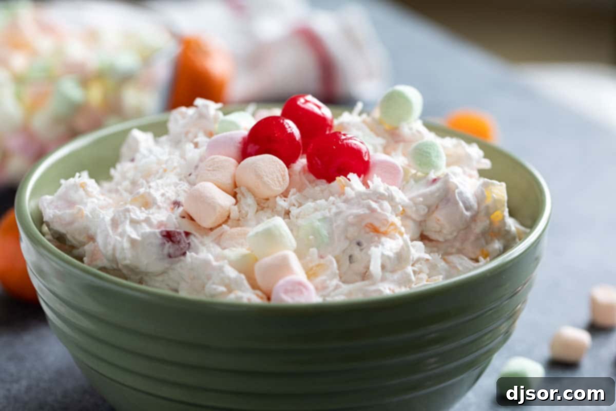 Classic Ambrosia Salad with Oranges, Pineapple, Coconut, Cherries, and Marshmallows A vibrant bowl of Ambrosia Salad, elegantly garnished with fluffy marshmallows, bright red maraschino cherries, and delicate shredded coconut, ready to be served.