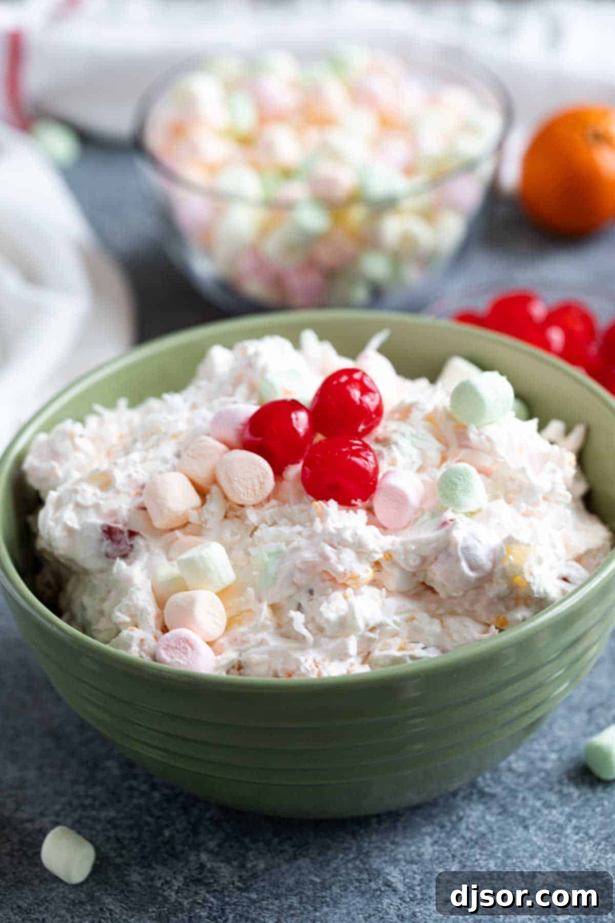 Finished Ambrosia Salad Topped with Cherries A vibrant green bowl brimming with Ambrosia Salad, generously topped with an array of bright red maraschino cherries, creating an inviting and colorful display.