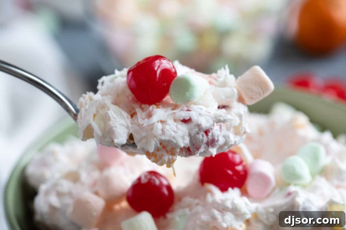 Spoonful of Ambrosia Salad A close-up shot of a spoon full of creamy Ambrosia Salad, showcasing the individual pieces of orange, pineapple, coconut, and marshmallows, ready for a delightful taste.
