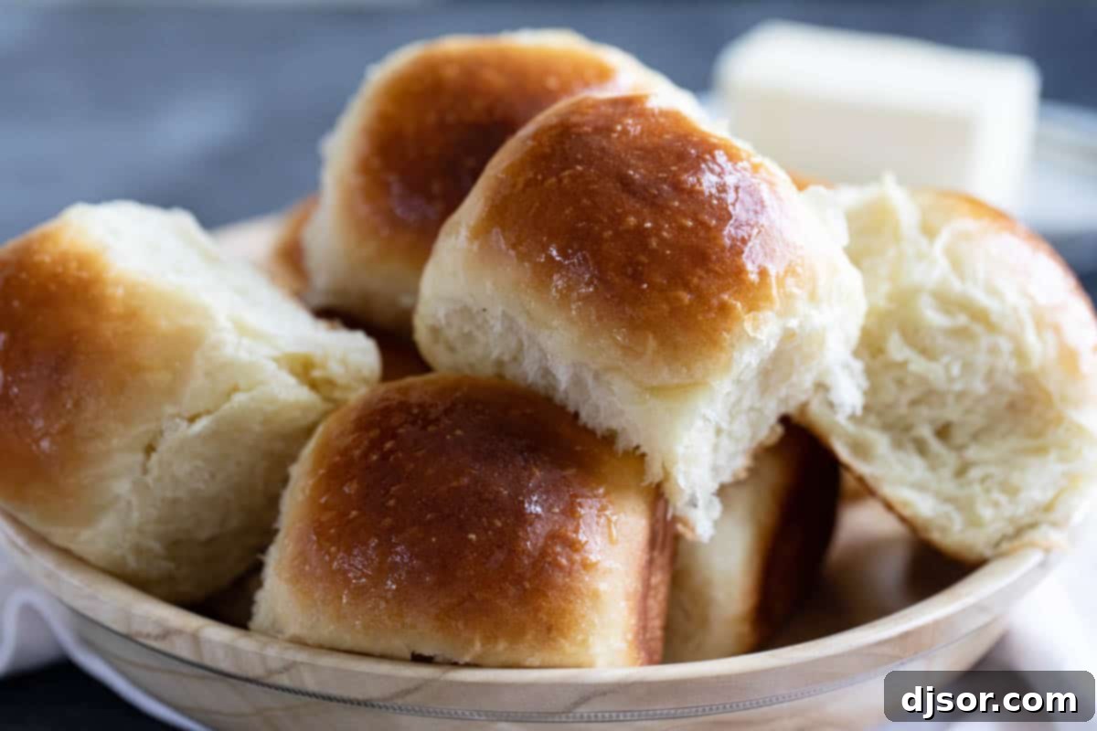 A large ceramic bowl filled with freshly baked, golden potato rolls, ready to be served.